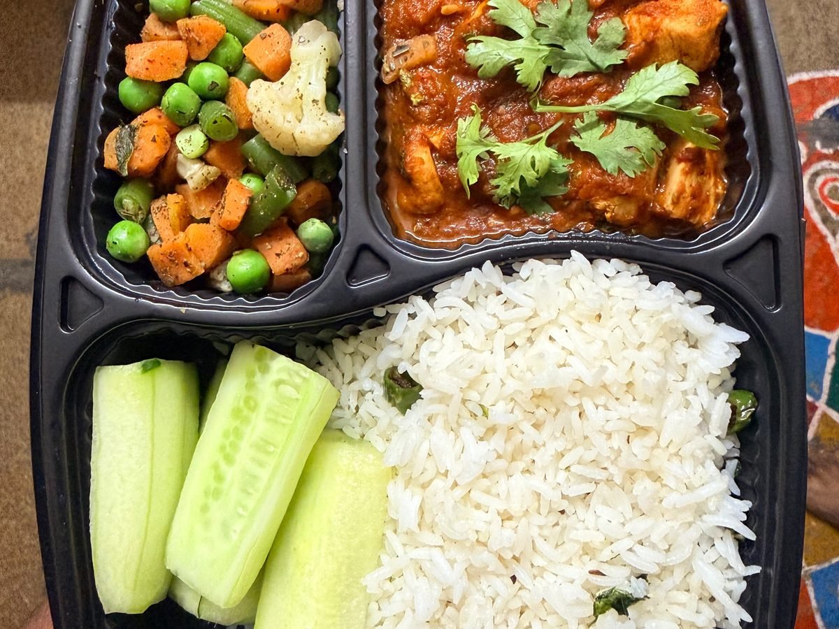 Paneer and jeera rice box: paneer masala, cumin rice, cucumber and mixed vegetables in a three-compartment tray